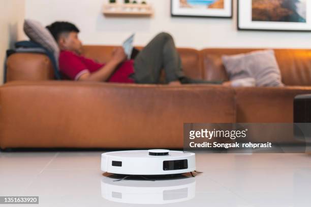 robot vacuum cleaners clean the room while the man lies on the sofa close-up. - robot vacuum stock pictures, royalty-free photos & images