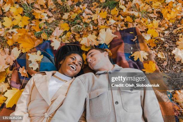mix raced couple laying on blanket in park in autumn - romantic picnic stockfoto's en -beelden