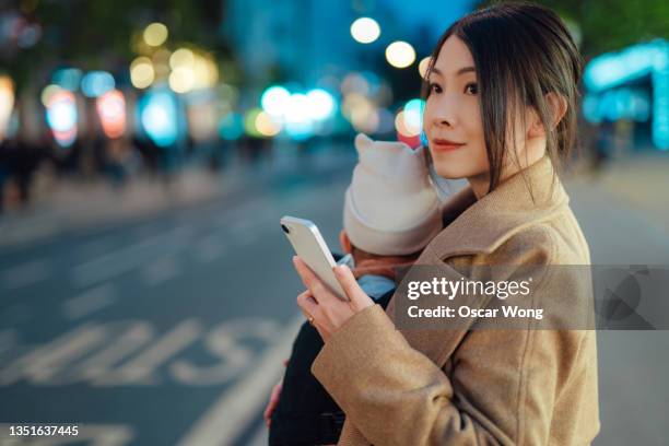 young asian mother using smart phone while carrying baby in the city - digital business london stockfoto's en -beelden