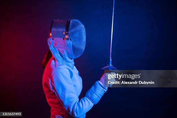 side view of a woman athlete swordsman in a helmet with an epee in the rays of neon. sports and fencing concept - escrime photos et images de collection