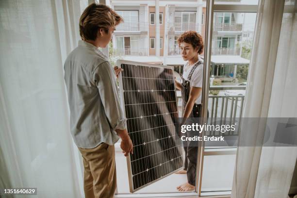 pareja gay asiática está instalando un panel solar en el balcón de la casa-foto de archivo - central eléctrica solar fotografías e imágenes de stock