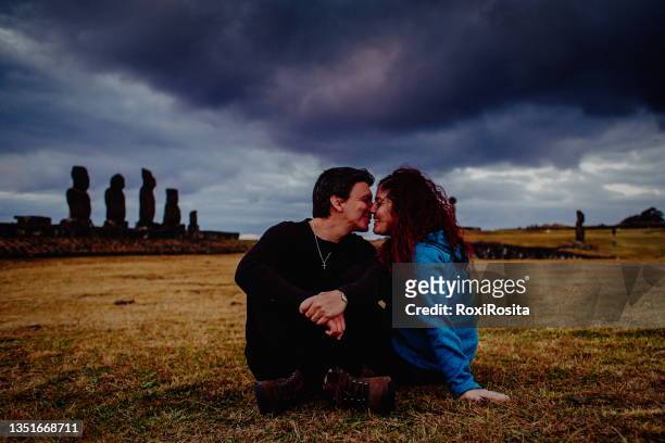 heterosexual couple sitting enjoying sunset on easter island with moai background - easter island fotografías e imágenes de stock