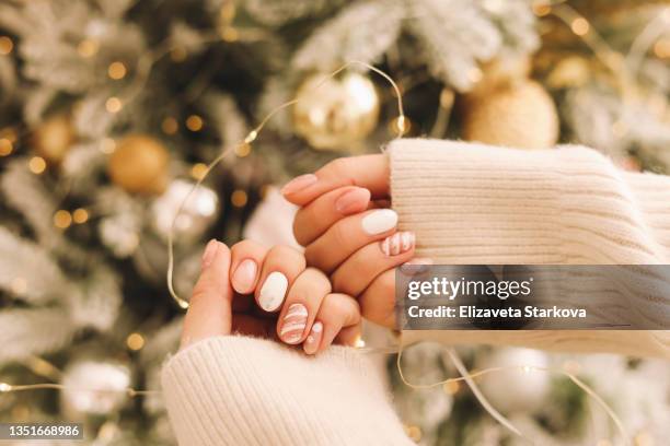 women's hands with a well-groomed manicure in a cozy sweater are preparing for the christmas holiday decorate the christmas tree with balloons and toys open a festive gift box new year at home indoor - manicure stockfoto's en -beelden