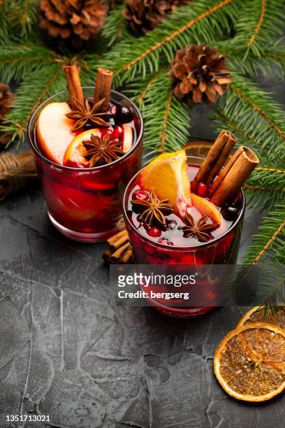 duas taças de vinho tinto mulled natalino com decoração, laranja, canela e árvore de abetos em fundo rústico - vinho quente - fotografias e filmes do acervo