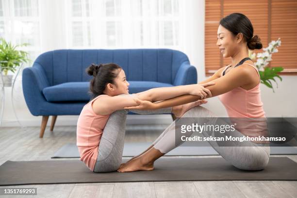 sportive family concept. adorable excited cheerful joyous beautiful step-sisters are doing sport limbering up together, they are sitting on mats trying to rich toes and feet - leg stretch girl stock pictures, royalty-free photos & images