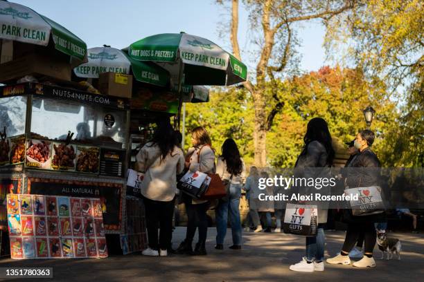 People carrying "I love NY" gift bags stand in line a food cart in Central Park on November 06, 2021 in New York City. People are enjoying cooler...