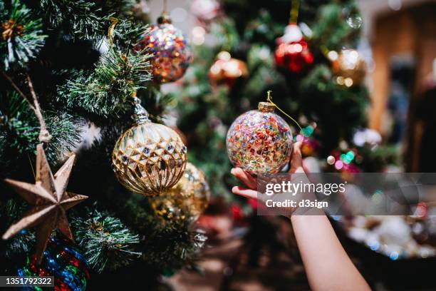 cropped shot of little girl's hand holding a colourful bauble, decorating and hanging on christmas tree in the festive christmas season. countdown to christmas. festival and celebration concept - christmas atmosphere stock pictures, royalty-free photos & images