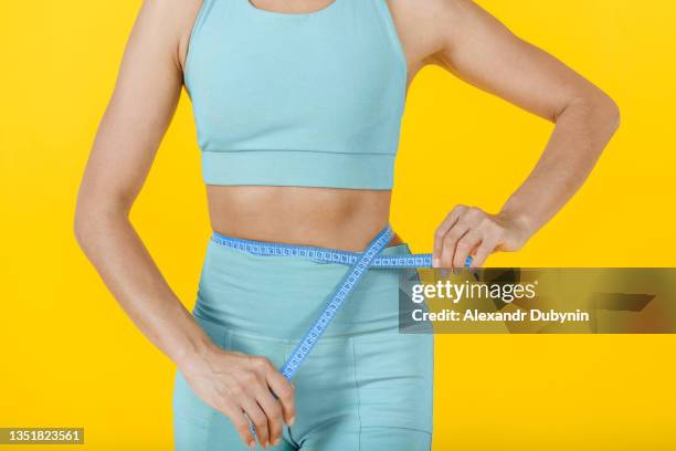 woman measures the body with a tape on a yellow background. diet concept - measuring tape stockfoto's en -beelden