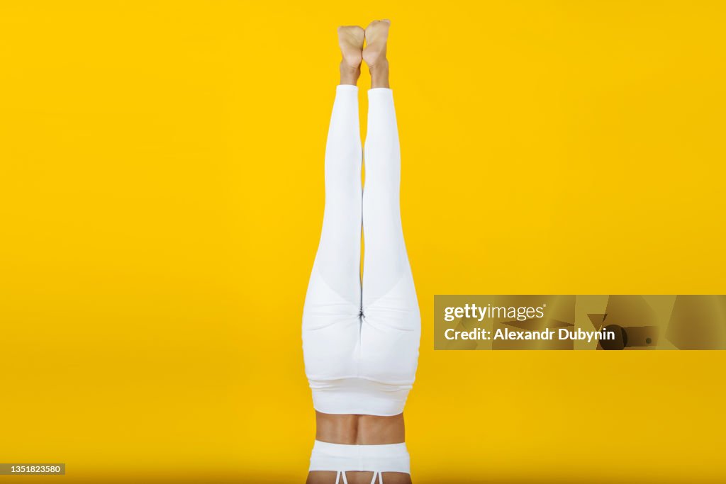 Inverted beautiful female legs in sportswear on a yellow background in the studio