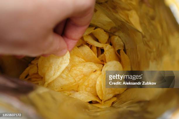 the girl takes crispy fried fatty potato chips from a package or pack. chips in the hands of a woman, she eats them. the concept of an unhealthy diet and lifestyle, the accumulation of excess weight. - fat guy foto e immagini stock