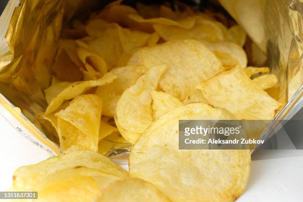 crispy fried greasy potato chips fall out or are spilled out of the package, on a white background or table. the concept of unhealthy diet and lifestyle, accumulation of excess weight. - bag of chips fotografías e imágenes de stock
