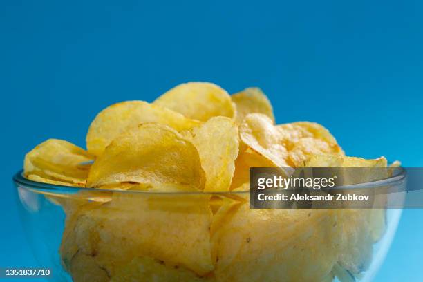 crispy golden fried fat potato chips in a glass bowl or plate on a bright background or table. the concept of unhealthy diet and lifestyle, the accumulation of excess weight. copy of the text space. - blue bowl fotografías e imágenes de stock
