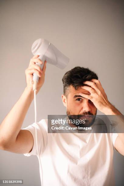 man blow drying hair against gray wall at home - man with gray hair stock pictures, royalty-free photos & images