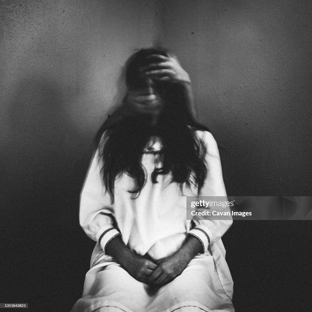 Creepy ghost girl sitting in chair with eerie hands grabbing her face