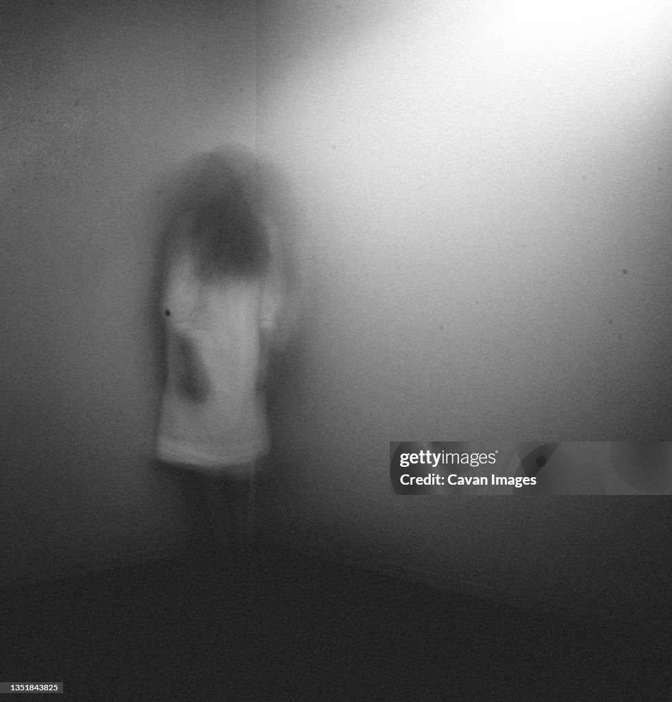 Ghost girl in white nightgown standing in corner of room at home