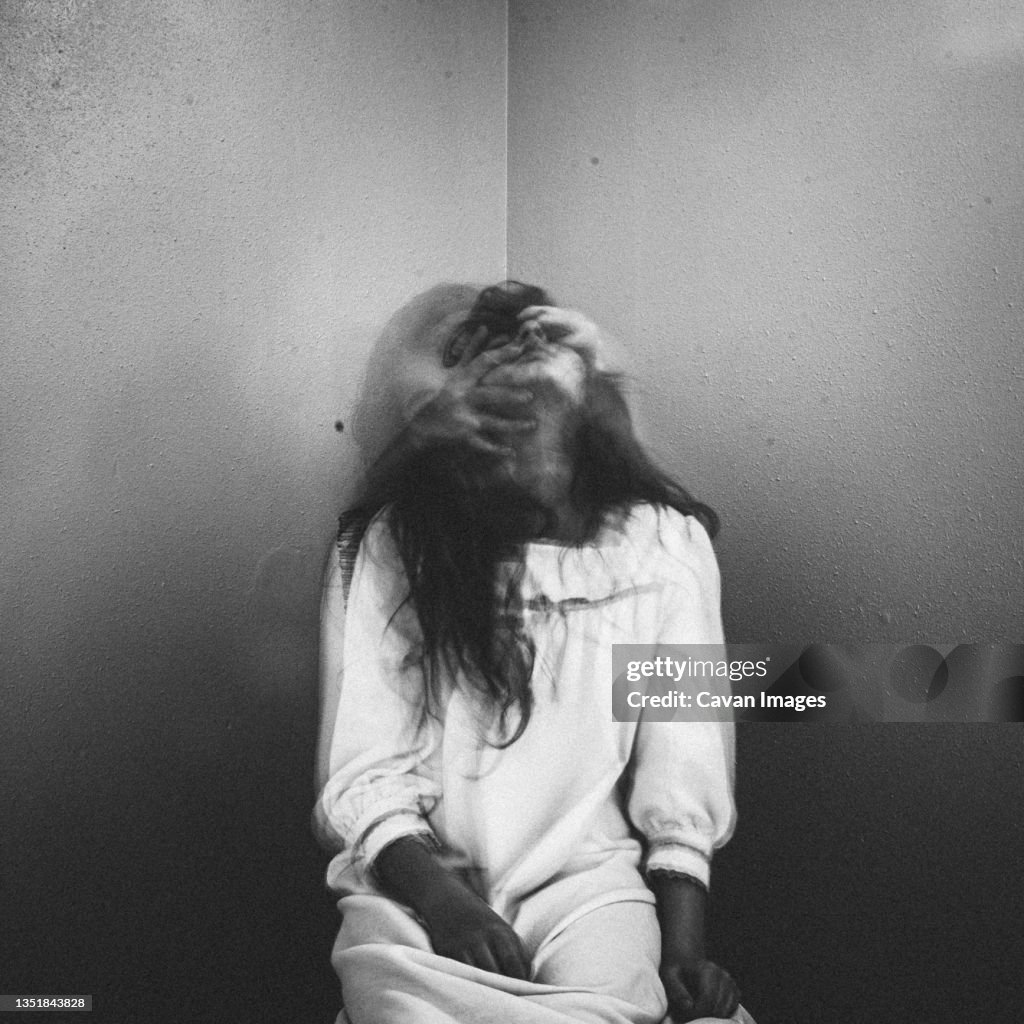 Spooky girl sitting in corner with hands pulling her face back