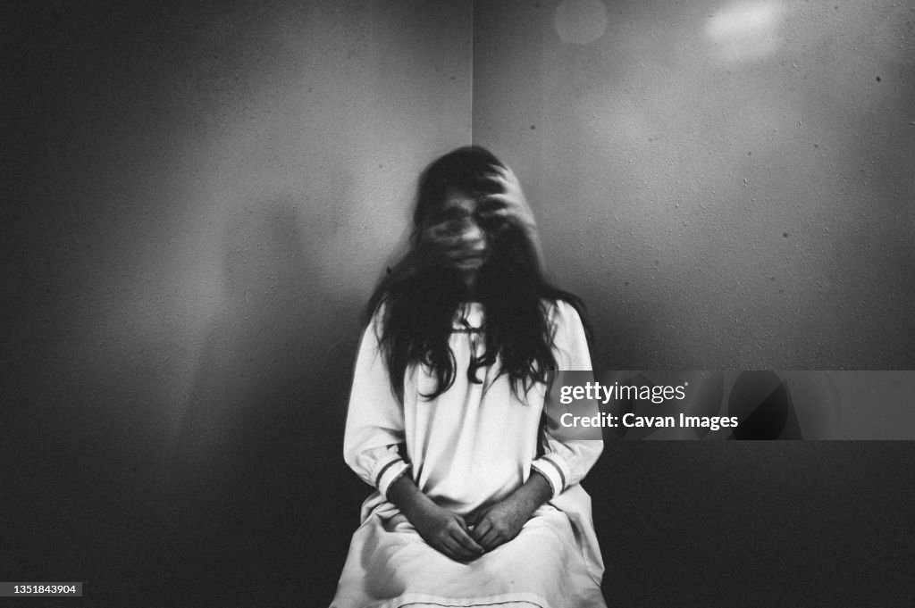 Creepy girl sits in chair with ghostly hands covering her face