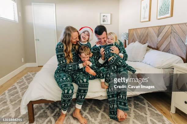 caucasian family in christmas pajamas snuggles on bed in phoenix home - pyjama stockfoto's en -beelden