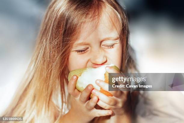 girl in the morning eating a pear in bed - child eating a fruit stock-fotos und bilder