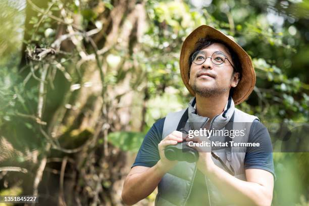 senior asian man watching bird while holding binocular in an eco forest camp. hobbies, nature addicted, and nature lover. - bird watching stock pictures, royalty-free photos & images