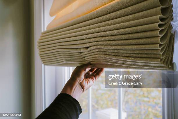 woman adjusts roman shade on window - closing stock pictures, royalty-free photos & images