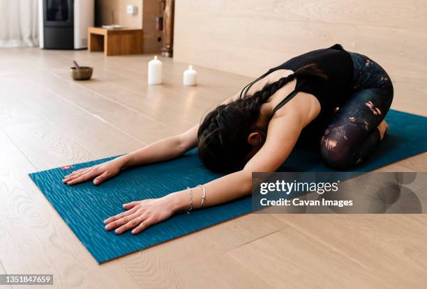 full length of a young woman sitting in child's pose on a yoga mat - yoga pose photos et images de collection