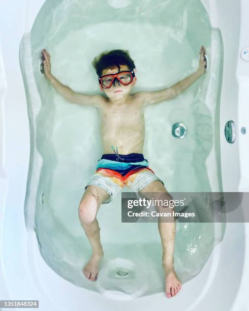 moody boy in a large bathtub wearing swim trunks and a diving mask - arlington virginia stock pictures, royalty-free photos & images