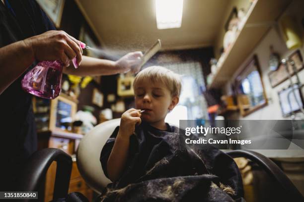 little boy enjoying a sucker during a haircut at a barber shop - barber shop 3 stock pictures, royalty-free photos & images