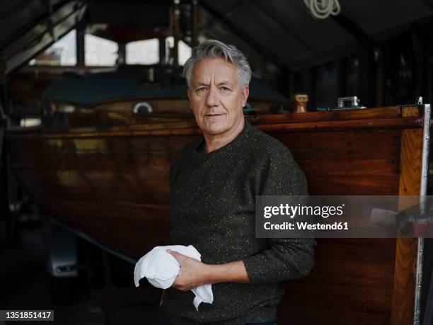 portrait of a senior man with cloth at wooden boat in a boathouse - boat old stock-fotos und bilder