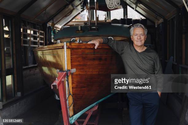 portrait of a proud senior man at wooden boat in a boathouse - rimessa per barche foto e immagini stock