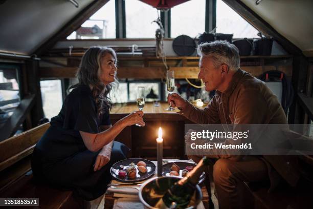 senior couple having a candlelight dinner on a boat in boathouse clinking champagne glasses - couple dinner stock-fotos und bilder