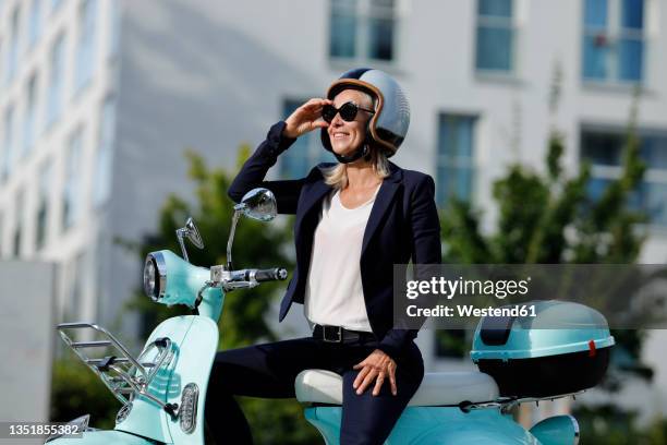 businesswoman adjusting sunglasses while sitting on motor scooter - roller stock-fotos und bilder