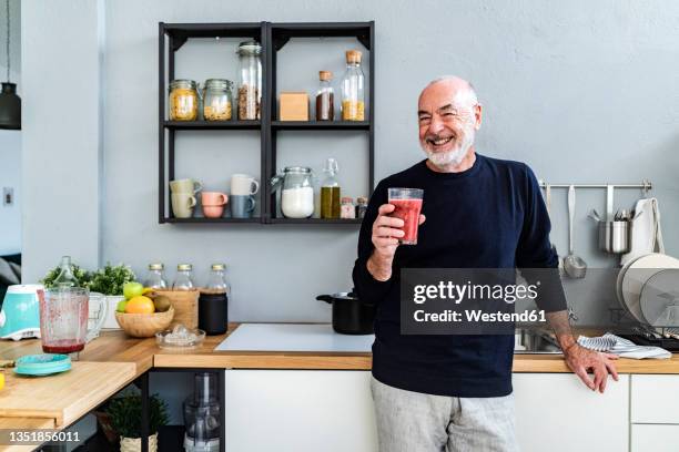 happy man holding smoothie glass in kitchen - blended drink stock pictures, royalty-free photos & images