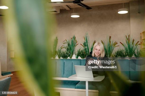 smiling businesswoman using smart phone while sitting in coworking office - co working stock-fotos und bilder