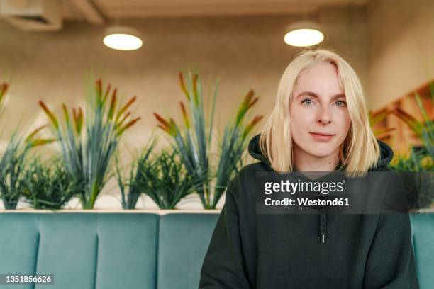 blond businesswoman with hooded shirt sitting in coworking office - kapuzenoberteil stock-fotos und bilder