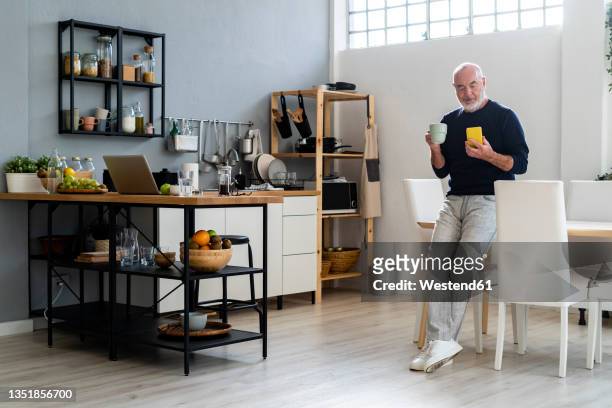 man having coffee while using mobile phone at home - phone leaning stock pictures, royalty-free photos & images