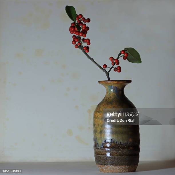 red dahoon berries arranged in an earthenware vase against bluish gray background - ikebana arrangement stock pictures, royalty-free photos & images