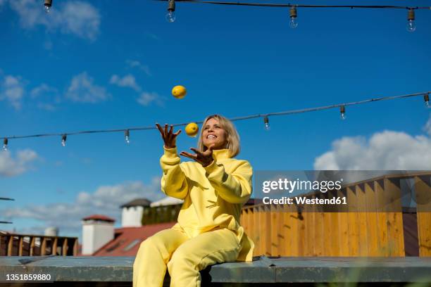 smiling woman juggling lemons while sitting on retaining wall - juggler stock-fotos und bilder