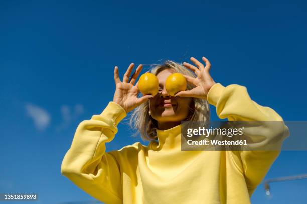 mid adult woman covering eyes with lemon during sunny day - limon fotografías e imágenes de stock