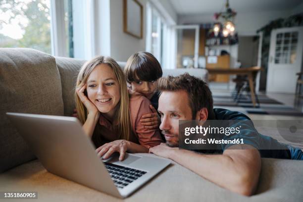 happy family lying on couch, using laptop - kinderheim stock-fotos und bilder