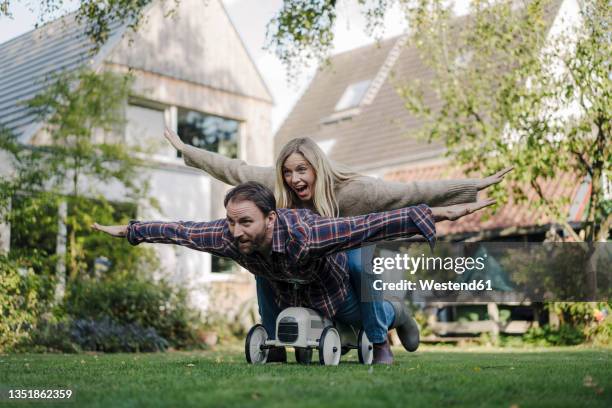 laughing couple, pretending to fly on a toy car in the garden - 飛行機のまね ストックフォトと画像
