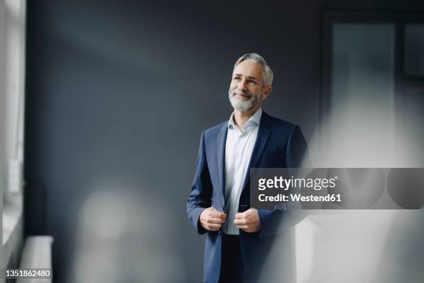 portrait of smiling mature businessman wearing blue suit in office looking at distance - office casual stock pictures, royalty-free photos & images