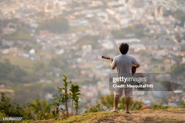 rear view of man playing guitar on the top of the mountain - humming stock pictures, royalty-free photos & images