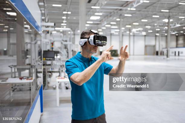 male professional gesturing while using virtual reality headset in factory - virtual reality stockfoto's en -beelden