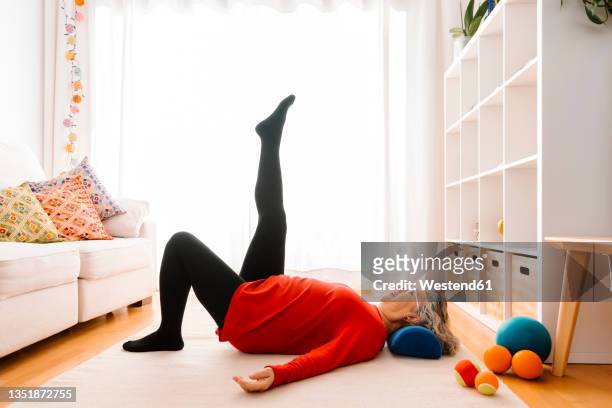 senior woman stretching leg while lying down at home - dar uma ajuda imagens e fotografias de stock