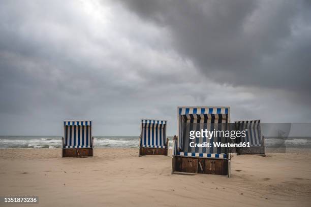 storm clouds over hooded beach chairs standing on empty beach - schleswig holstein stock pictures, royalty-free photos & images