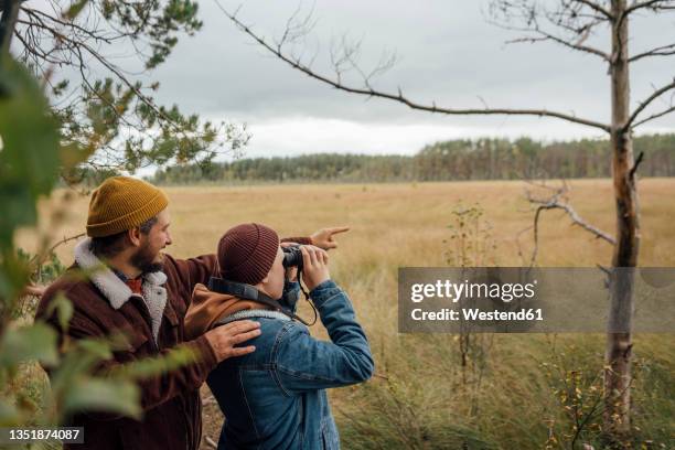 father pointing while standing by boy bird watching through binoculars in forest - bird watching stock pictures, royalty-free photos & images