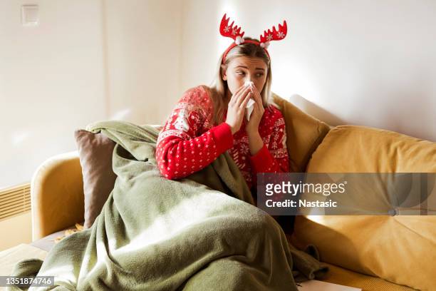 woman suffering from cold, lying in bed under blanket with tissue during christmas holidays - quarantine christmas stock pictures, royalty-free photos & images