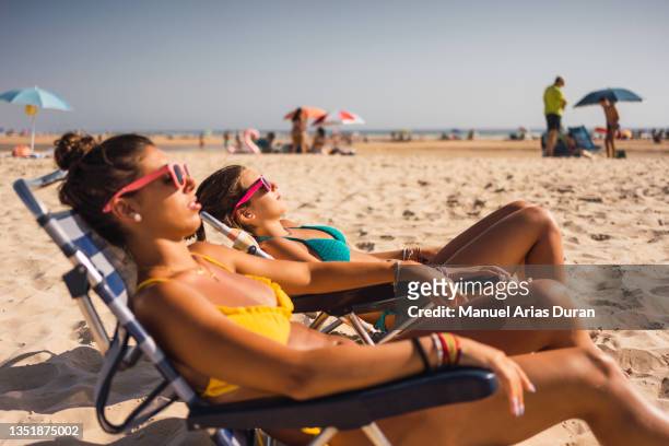 two friends sunbathing at the beach - sunbathing stockfoto's en -beelden