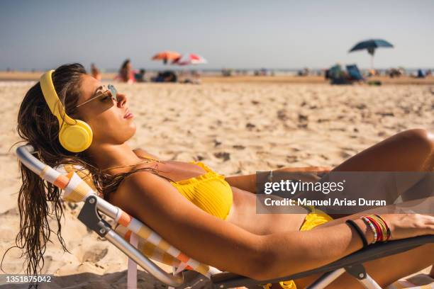 girl lying on the beach sunbathing while listening to music with wireless headphones - young woman beach stockfoto's en -beelden